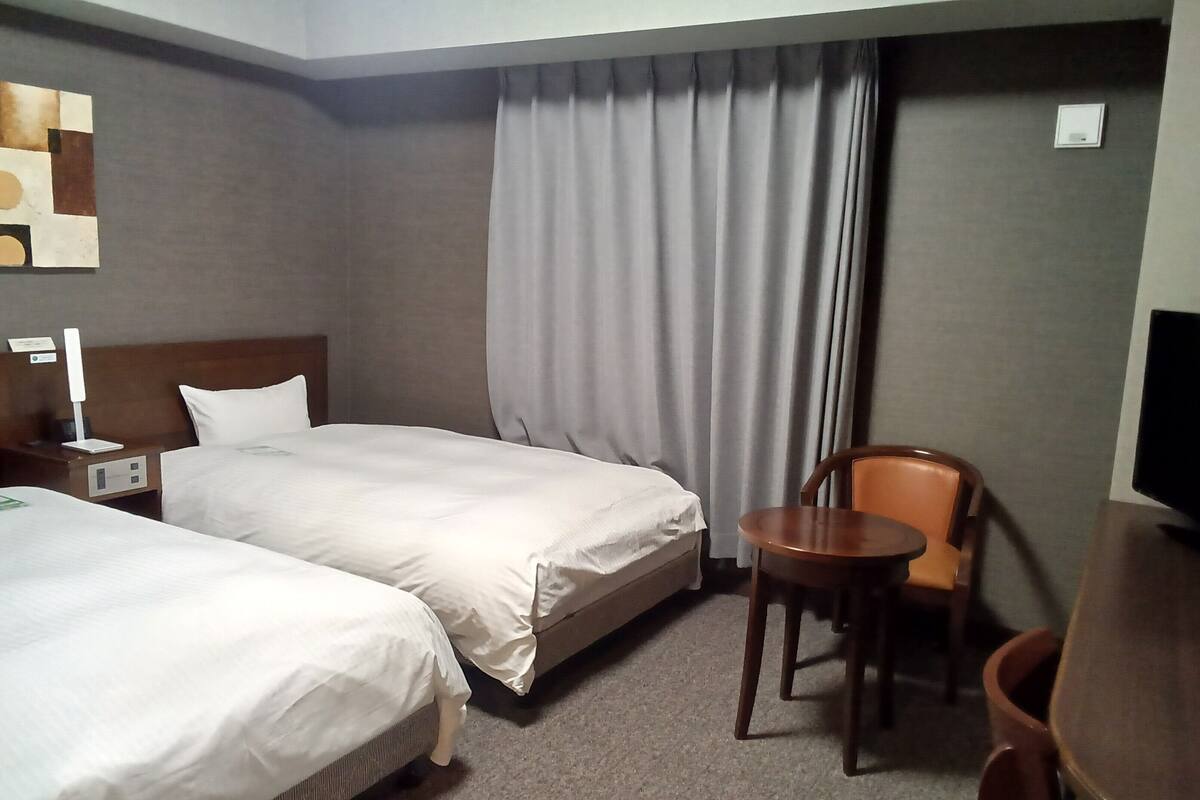 Une chambre d’hôtel avec deux lits, un bureau, une chaise et un téléviseur.