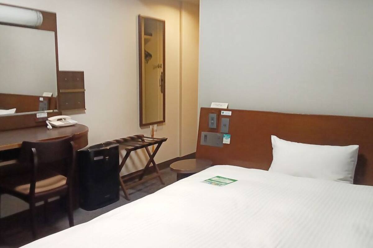 Une chambre d’hôtel équipée d’un lit, d’un bureau, d’une chaise, d’un miroir et d’une poubelle.