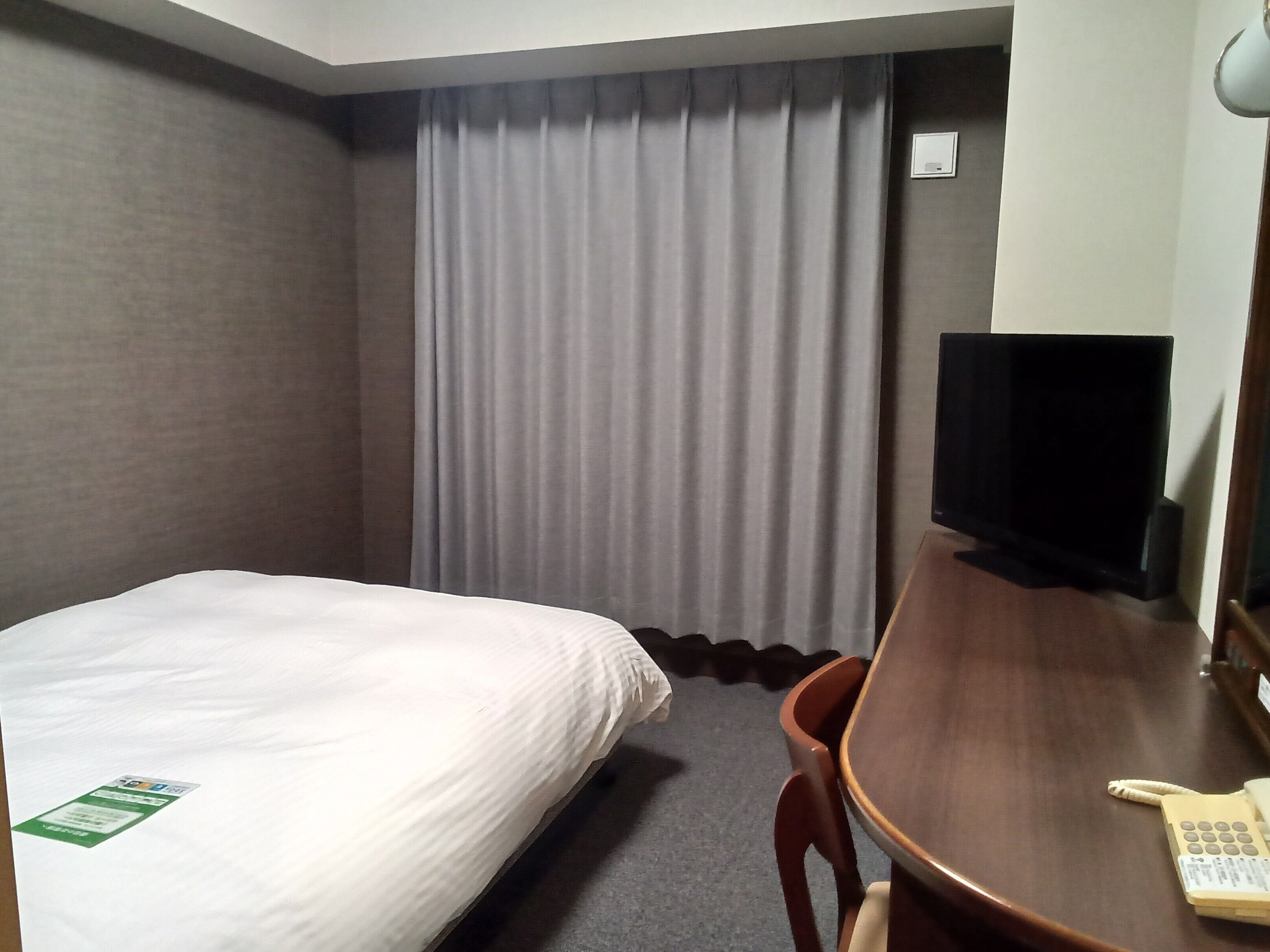 A hotel room with a bed, a desk with a telephone, a television, and a curtain.