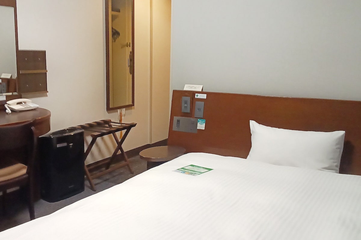 Une chambre d’hôtel comprenant un lit, un bureau avec un téléphone, une chaise, une poubelle et un miroir.