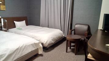 Habitación de hotel con dos camas, una silla, una mesita y un televisor.