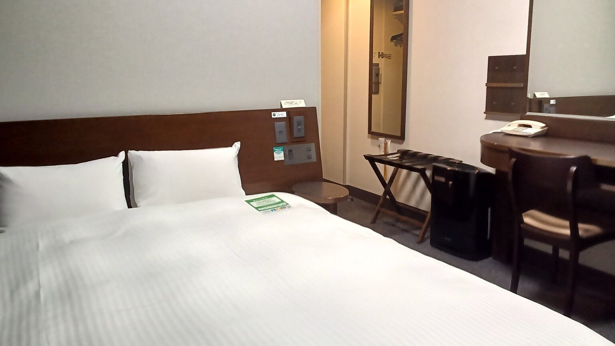 A hotel room with a bed, a desk, a chair, a telephone, and a mirror.