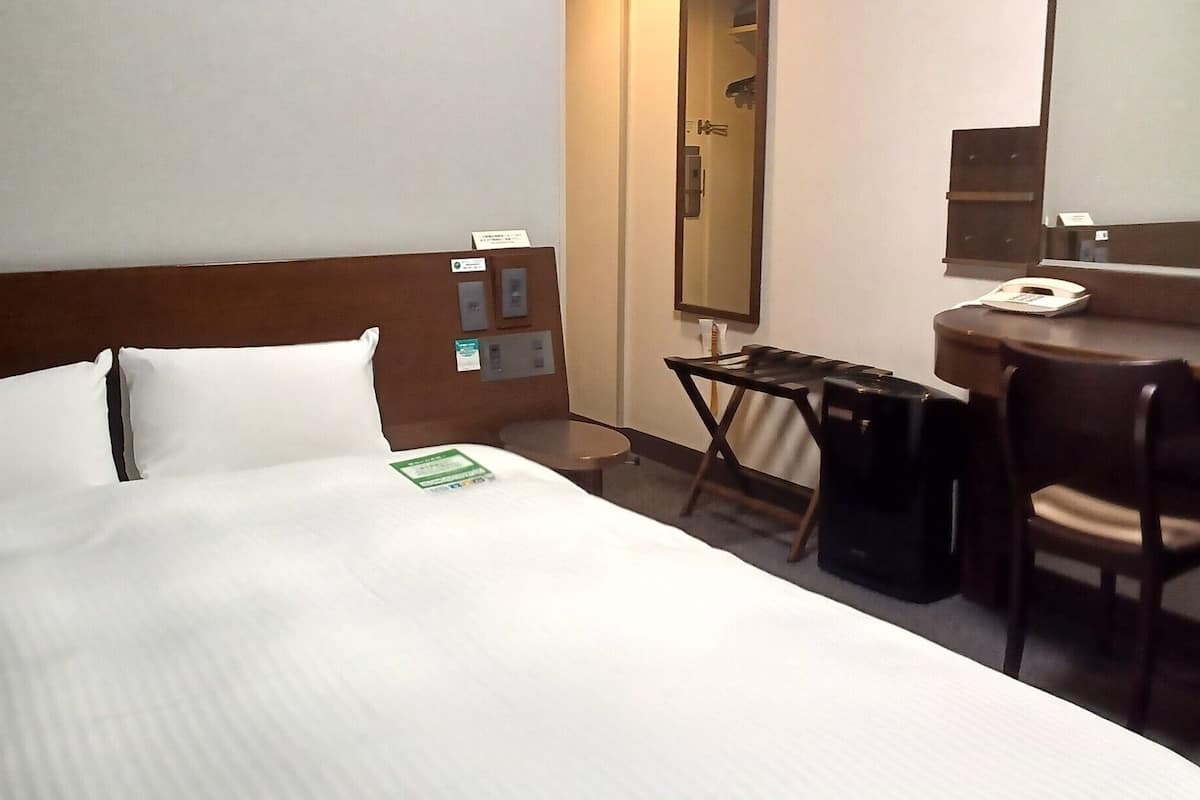 Habitación de hotel con cama, escritorio, silla, teléfono y espejo.