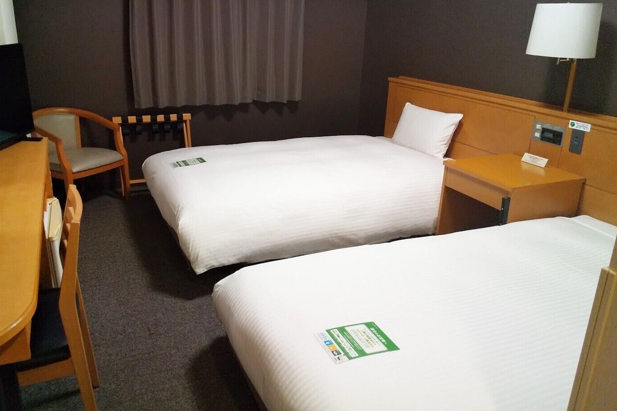 A hotel room with two beds, a desk with a chair, a TV, and a lamp.