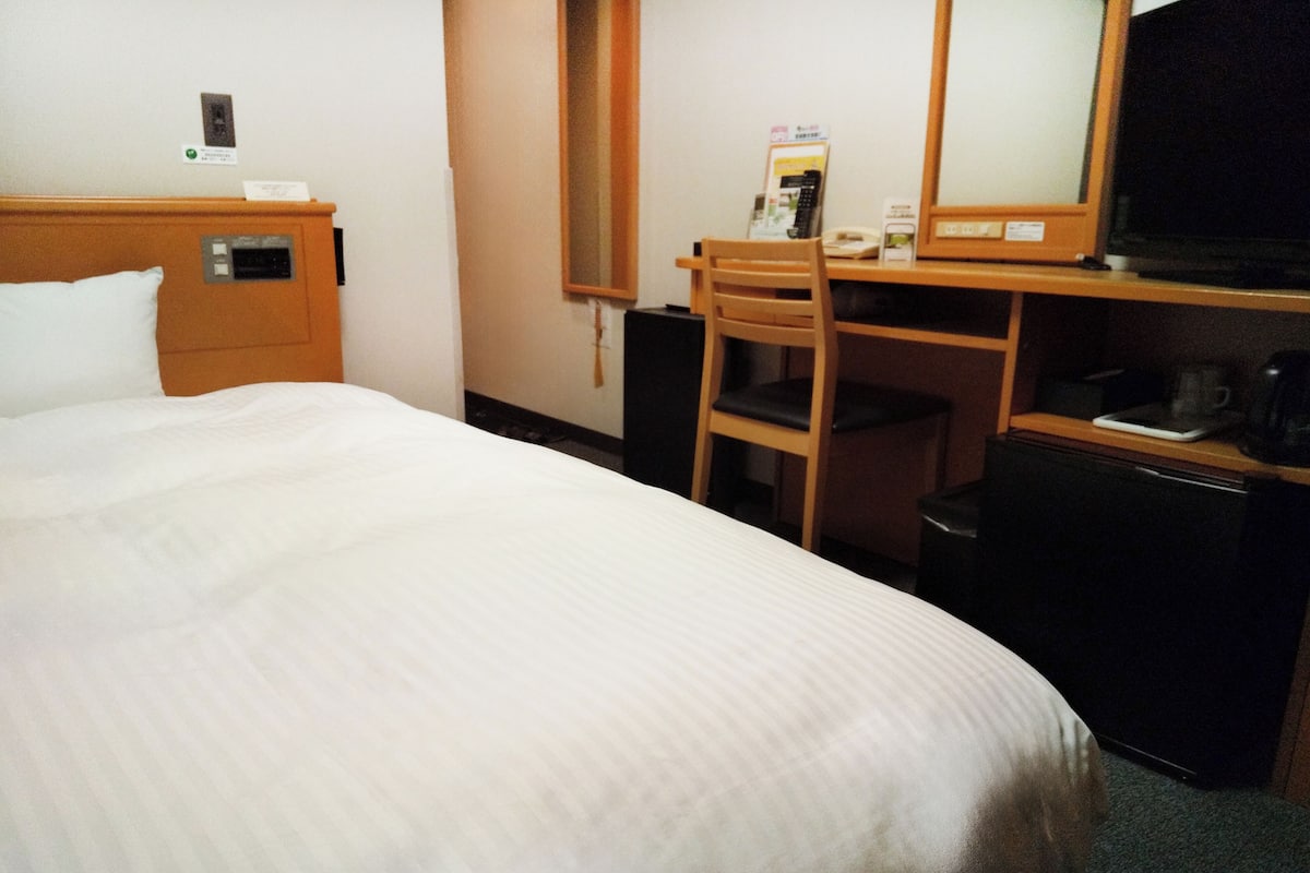A hotel room with a bed, a desk with a chair, a television, and a coffee maker.