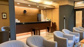 Un espace d’accueil d’hôtel avec un comptoir en bois, une horloge et des sièges disposés autour d’une petite table.