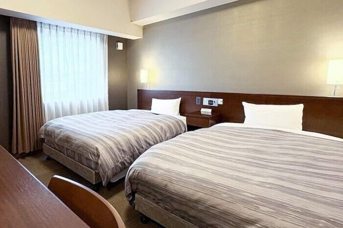 Ein Hotelzimmer mit zwei Einzelbetten, einem Holzkopfende, einem Schreibtisch und einem Fenster mit Vorhängen.