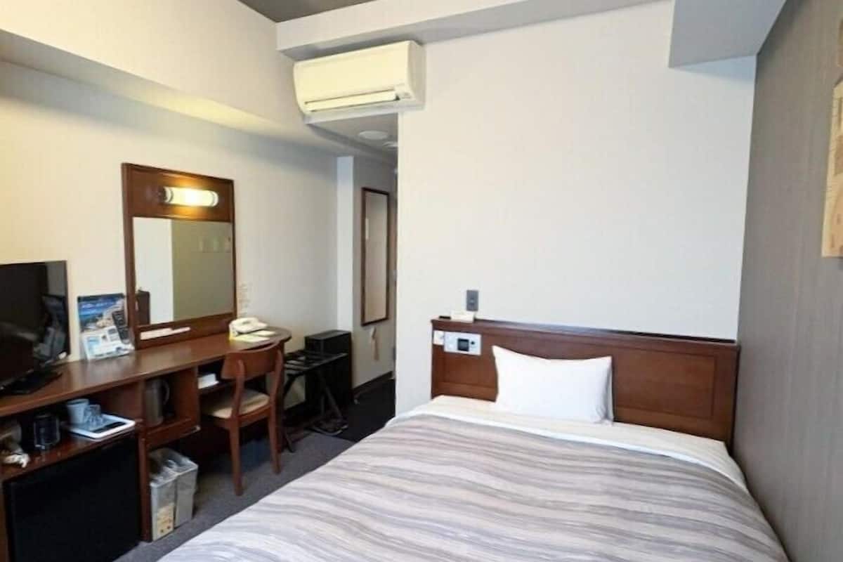 Ein Hotelzimmer mit Bett, Schreibtisch, Stuhl, Fernseher und Klimaanlage.