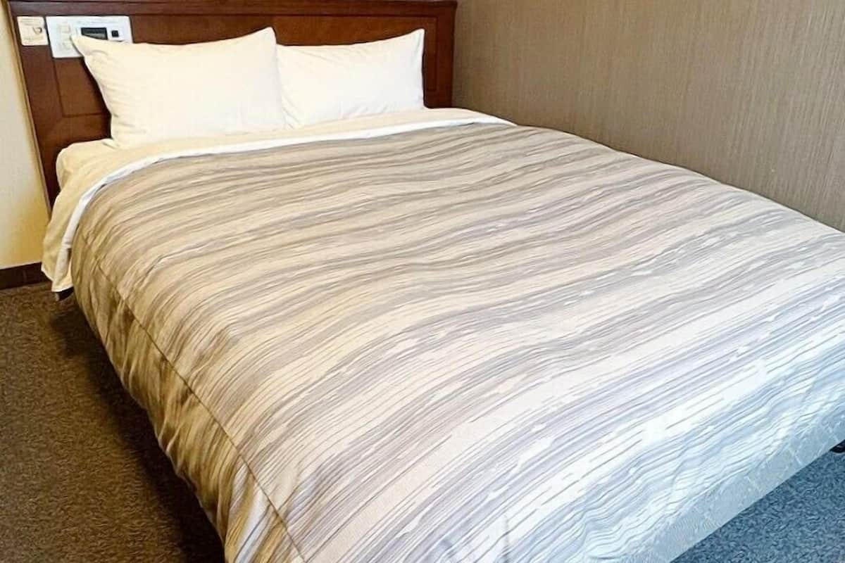 Ein Hotelzimmer mit einem hölzernen Kopfteil, einem Bett mit gestreifter Bettdecke und einem Teppichboden.