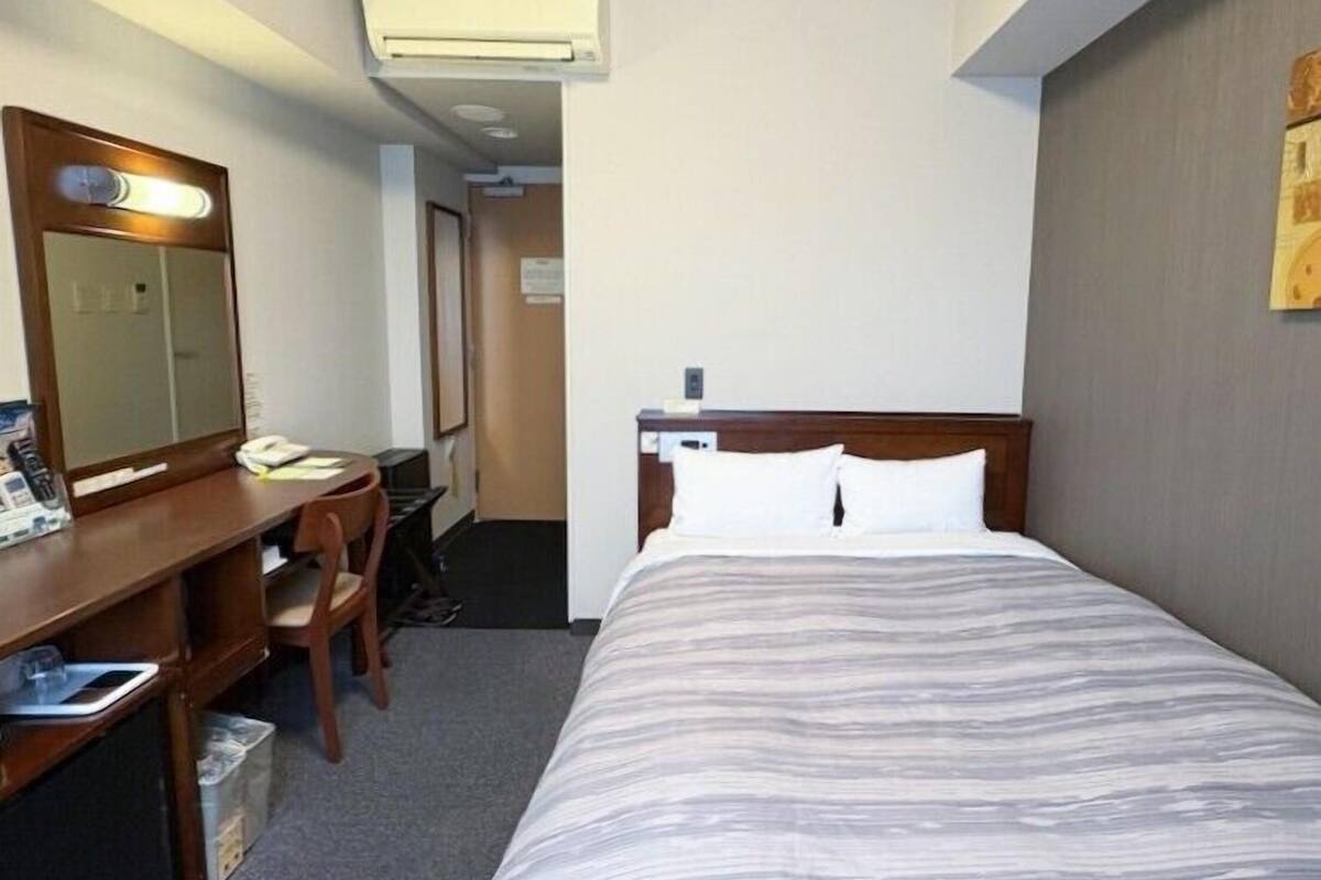 Ein Hotelzimmer mit einem Bett, einem Schreibtisch mit Stuhl, einem Spiegel und einer Klimaanlage.