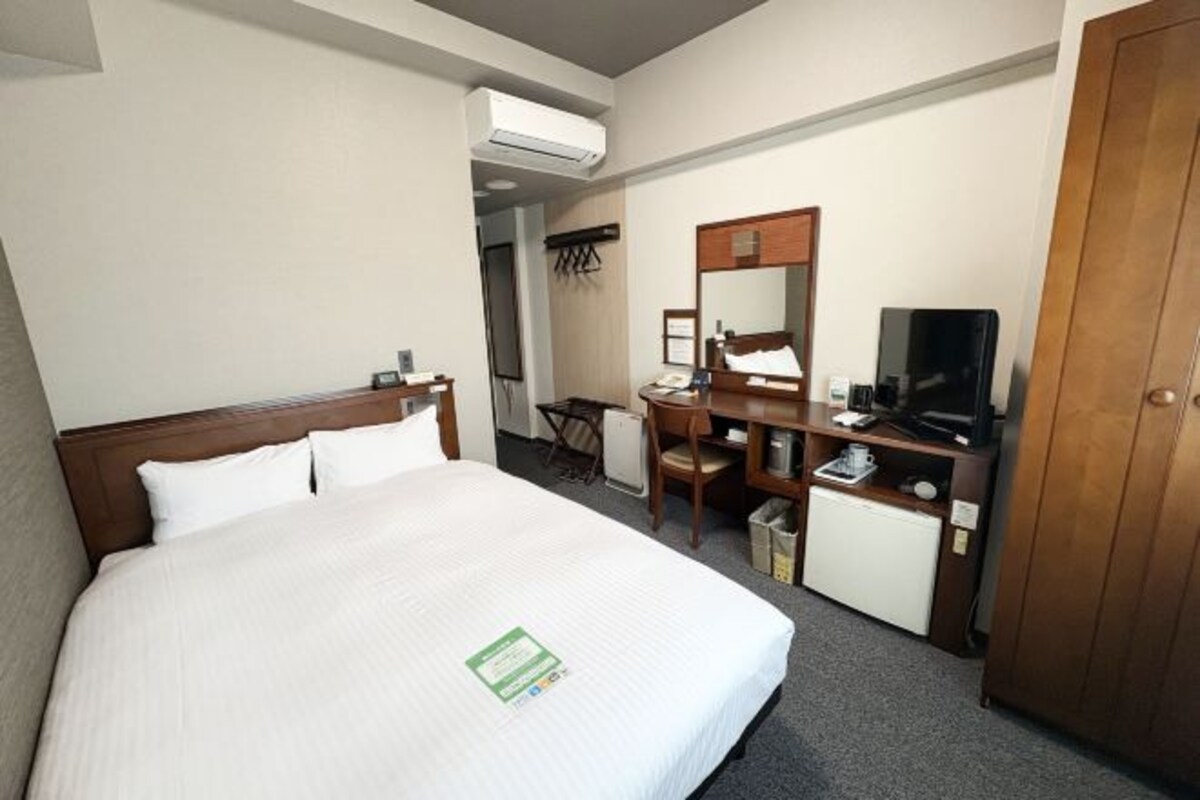A hotel room with a bed, a desk, a chair, a television, and a wardrobe.
