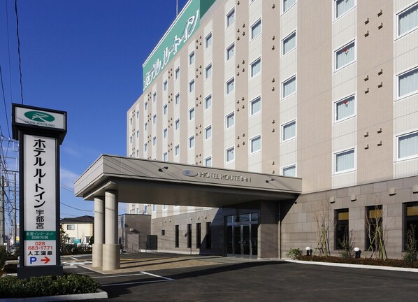 Un hotel de varios pisos con fachada moderna, entrada cubierta y un cartel que indica un área de estacionamiento.