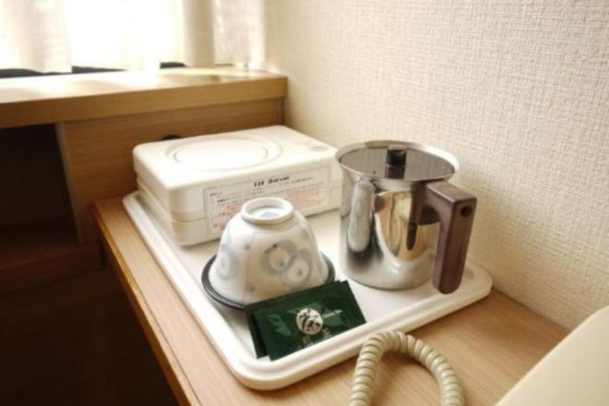 A hotel room with a wooden nightstand, a white telephone, a coffee maker, and a small green card.