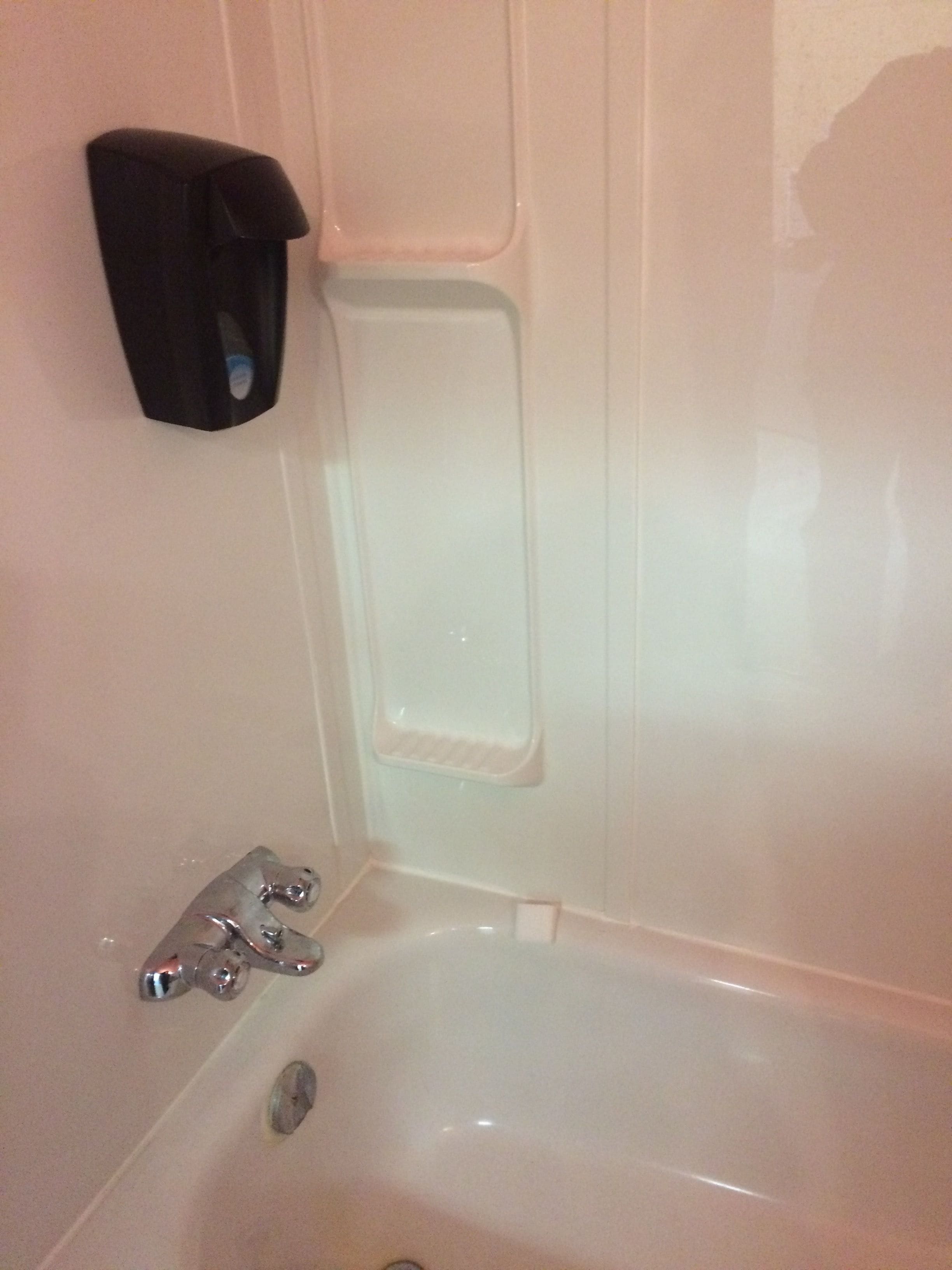 A bathroom with a bathtub, a hand dryer, and a soap dispenser mounted on the wall.