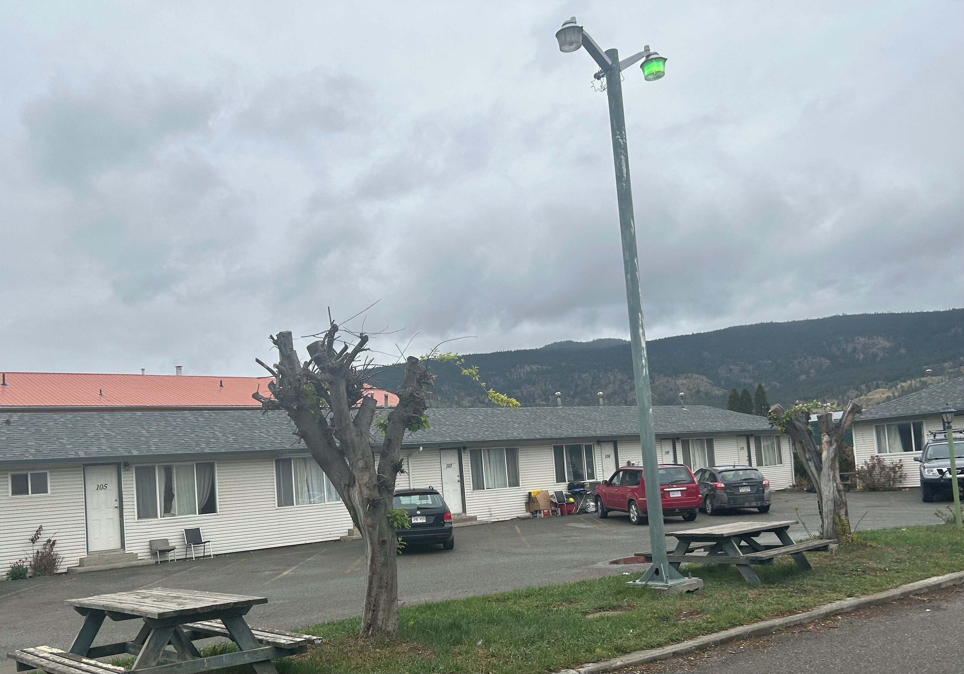 Un motel con techo rojo, una mesa de picnic y un estacionamiento con coches.