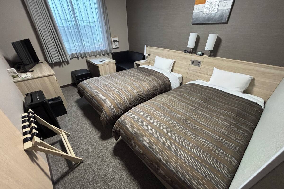 A hotel room with a large bed, a desk, a chair, a TV, and a window with curtains.