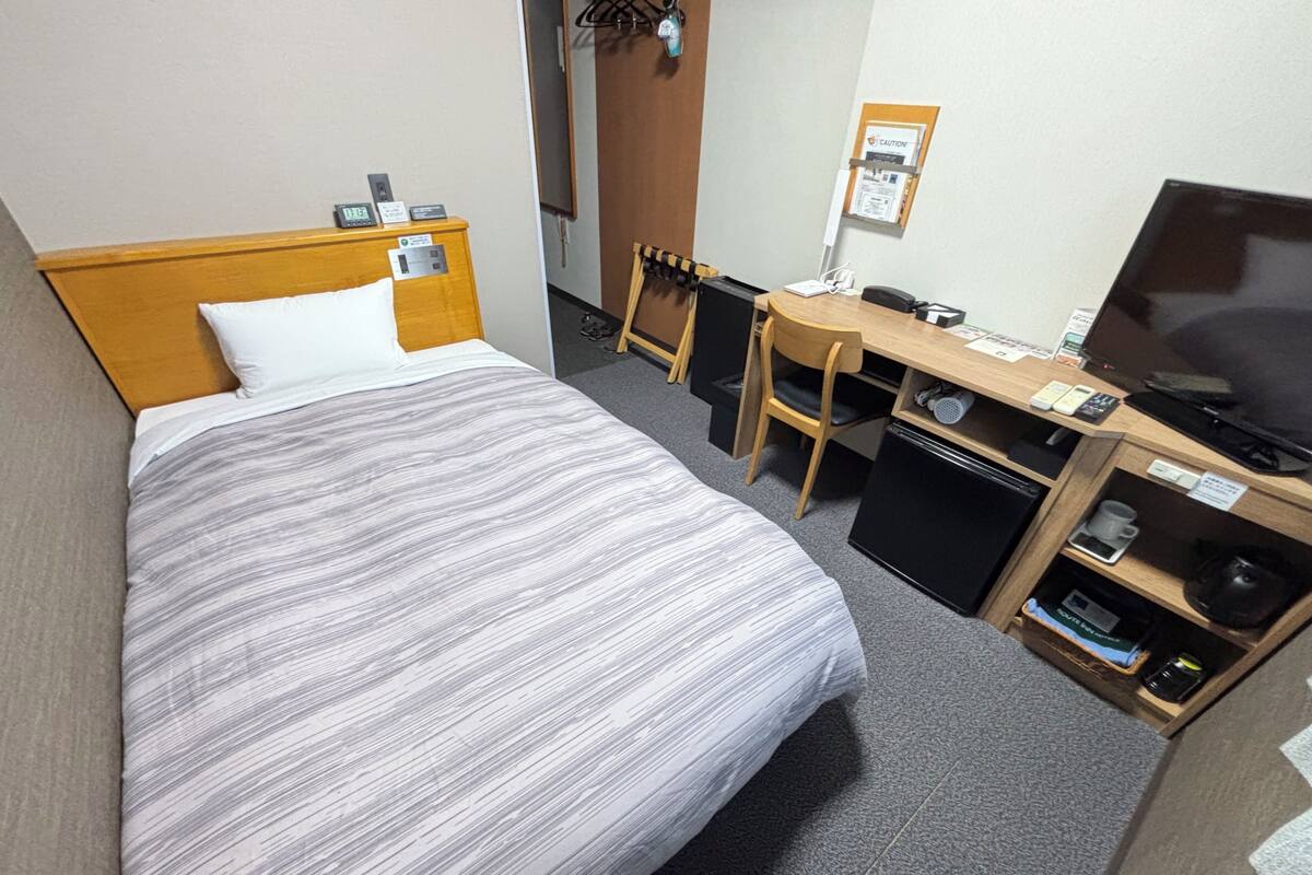 A hotel room with a bed, a desk with a computer, a television, and a small refrigerator.