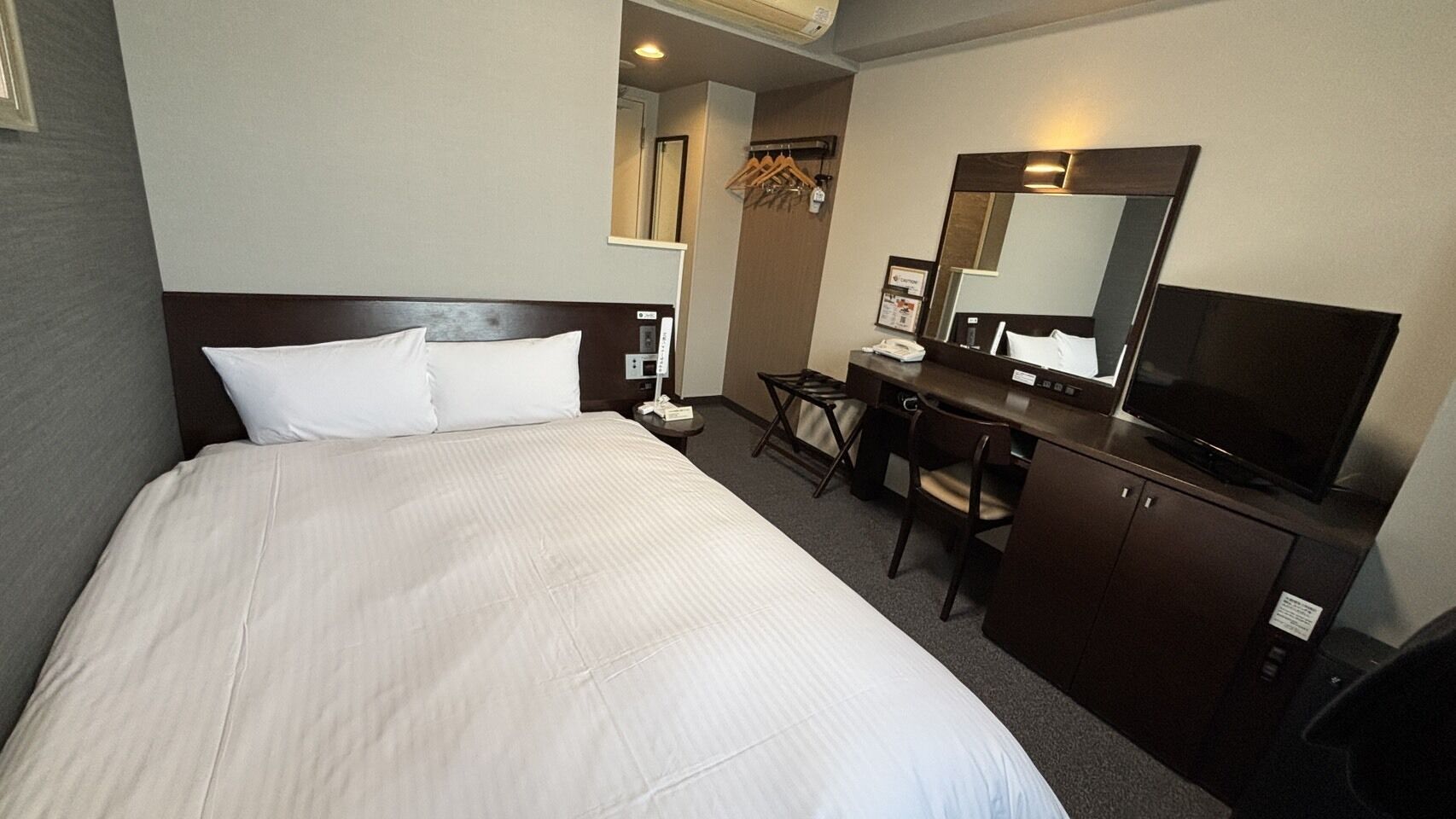 Une chambre d’hôtel avec un grand lit, un bureau avec une chaise, une télévision, un miroir et une armoire.