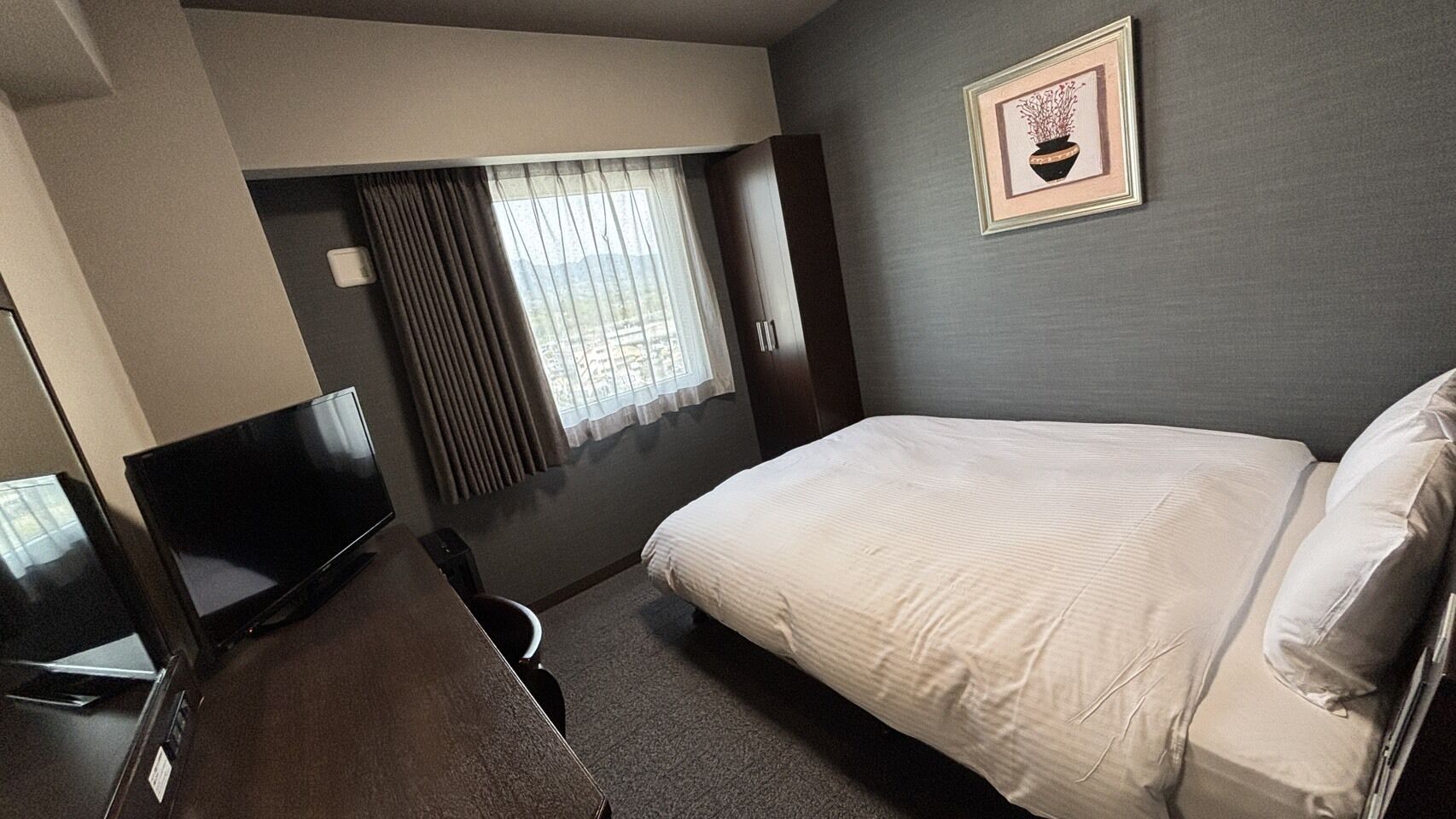 Une chambre d’hôtel avec un lit, une télévision, un bureau et une fenêtre avec des rideaux.