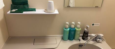 A bathroom with a sink, mirror, and toiletries including shampoo and conditioner.