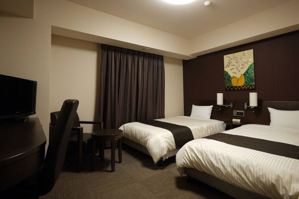 Habitación de hotel con dos camas, un escritorio, una silla, un televisor y un cuadro en la pared.