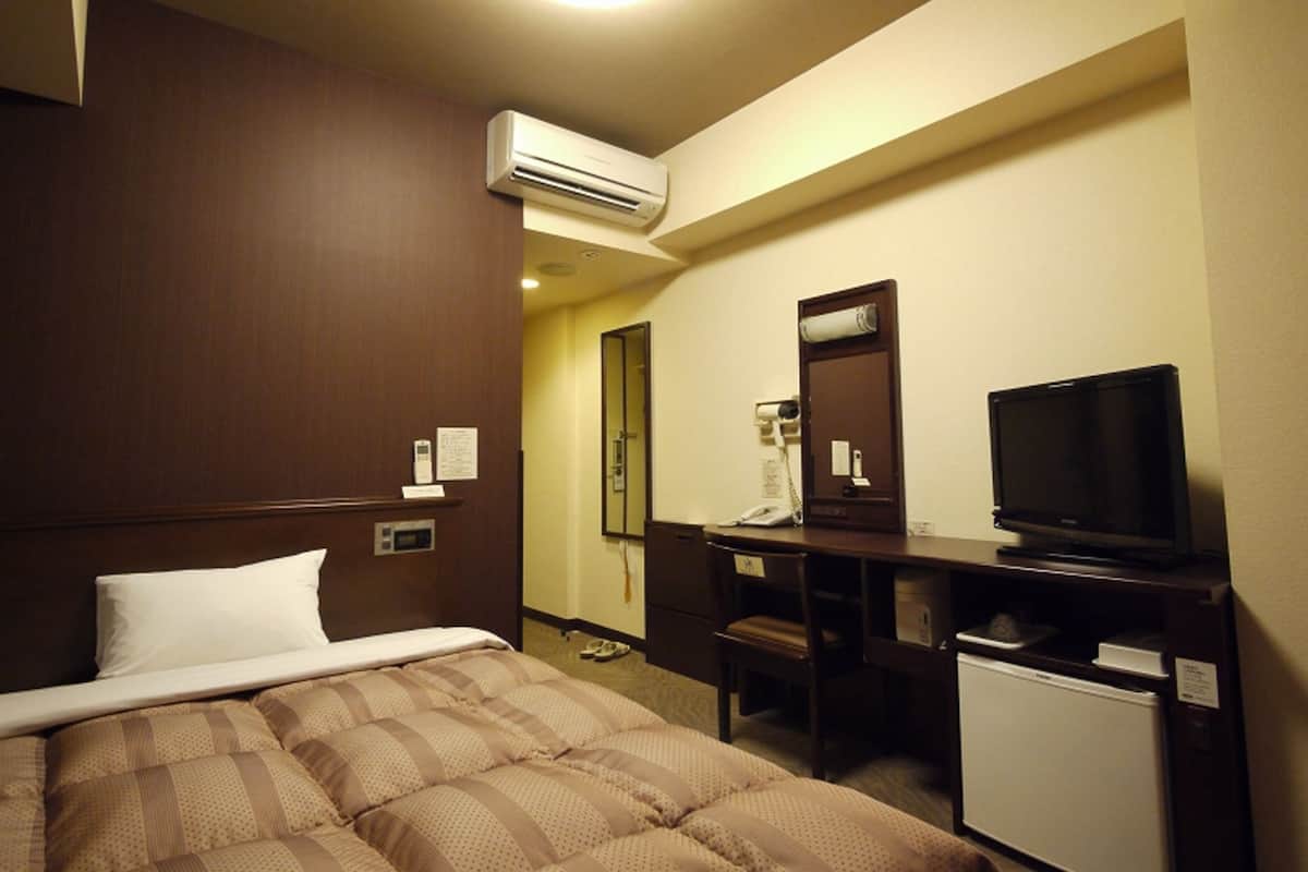 Habitación de hotel con cama, escritorio con televisor, refrigerador pequeño y aire acondicionado.