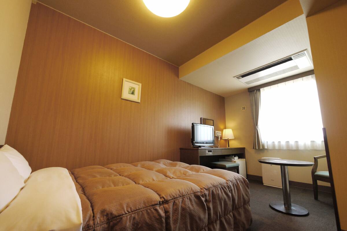 A hotel room with a bed, a desk, a television, and a window with curtains.