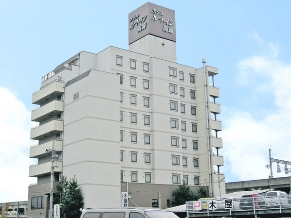 A multi-story hotel with a prominent sign at the top, multiple balconies, and a parking area in front.