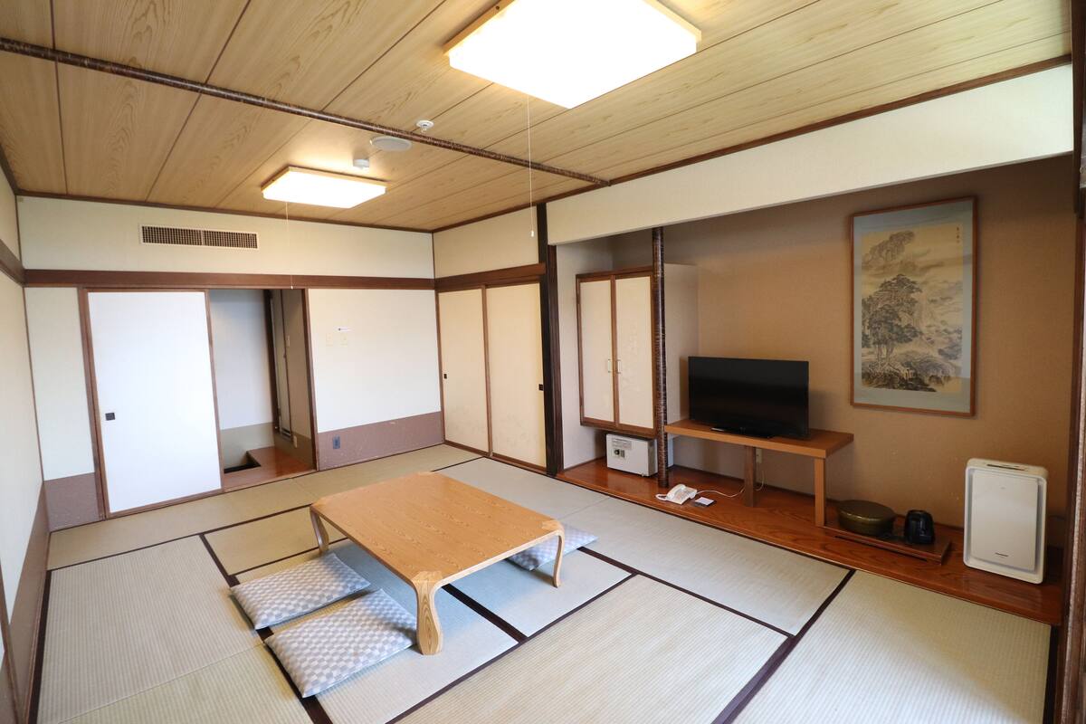 A traditional Japanese room with tatami flooring, a low wooden table, a television, and sliding doors.