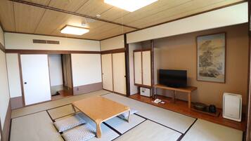 Una habitación japonesa tradicional con suelo de tatami, una mesa de madera baja, un televisor y puertas correderas.