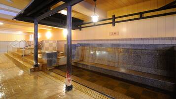 A public bath area with tiled floors, a stone bench, and a wooden structure with a light fixture.