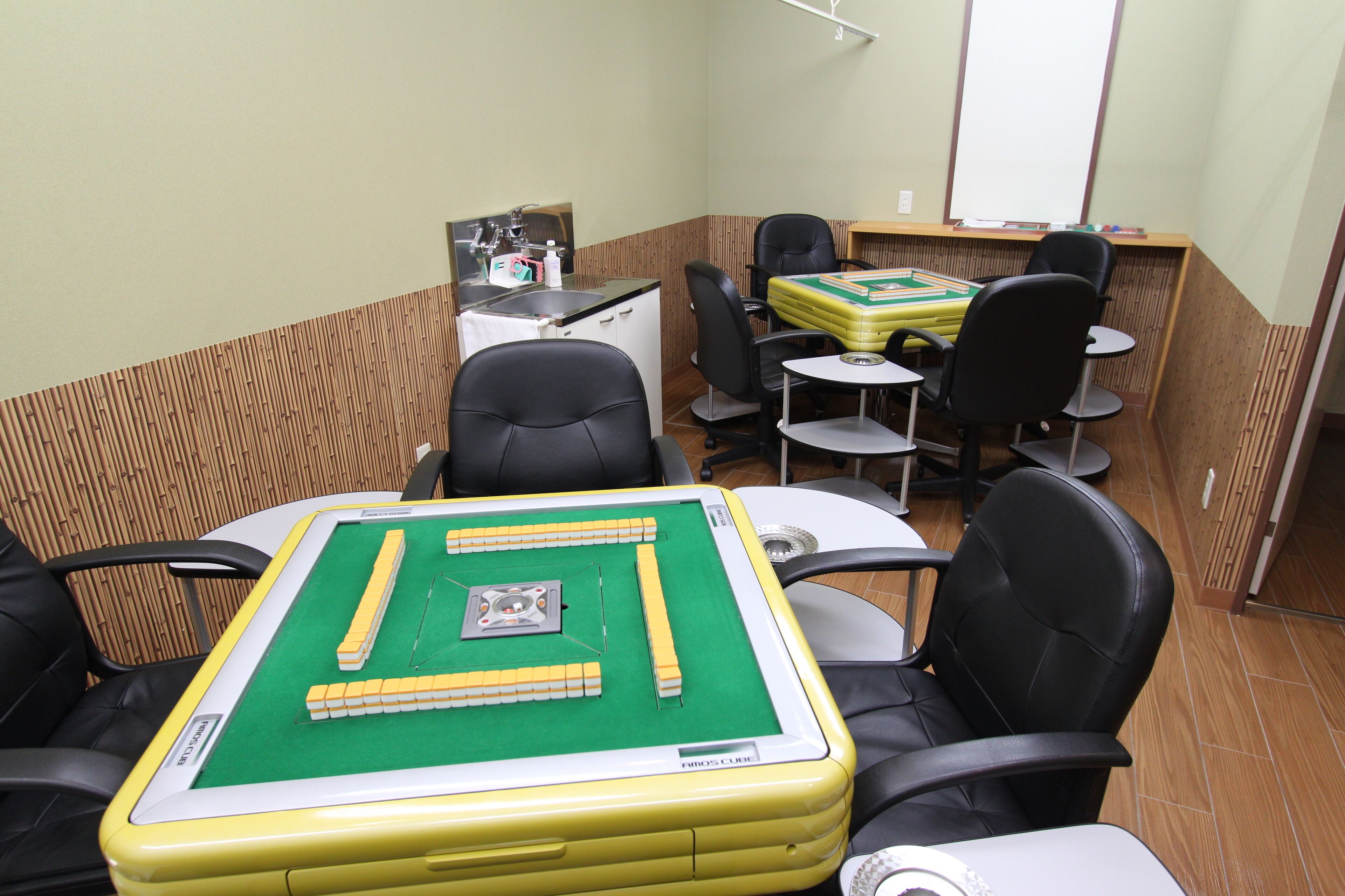 A room with a green pool table, black chairs, and a small white table with a yellow tablecloth.