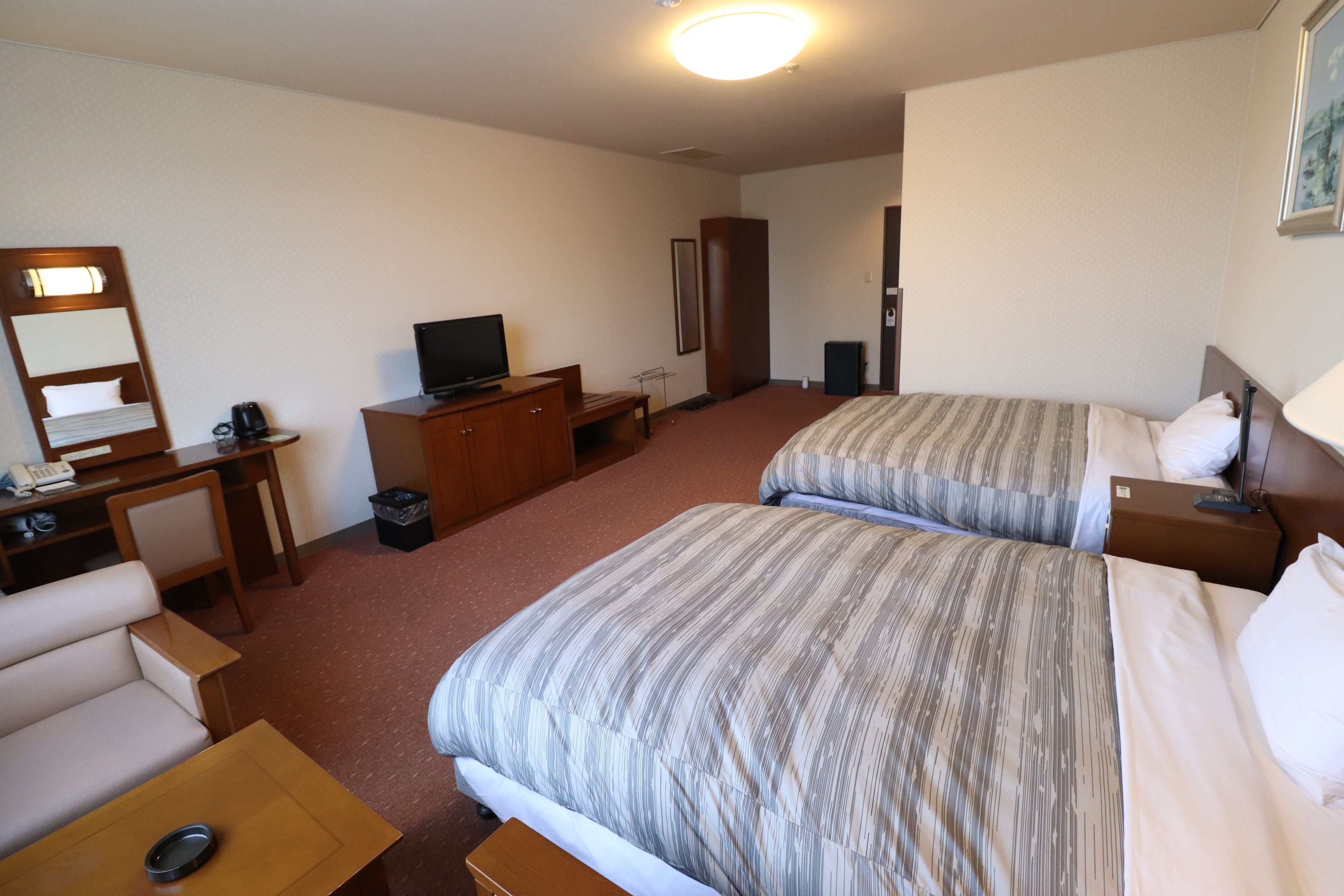 A hotel room with two beds, a desk, a chair, a television, and a bedside table.