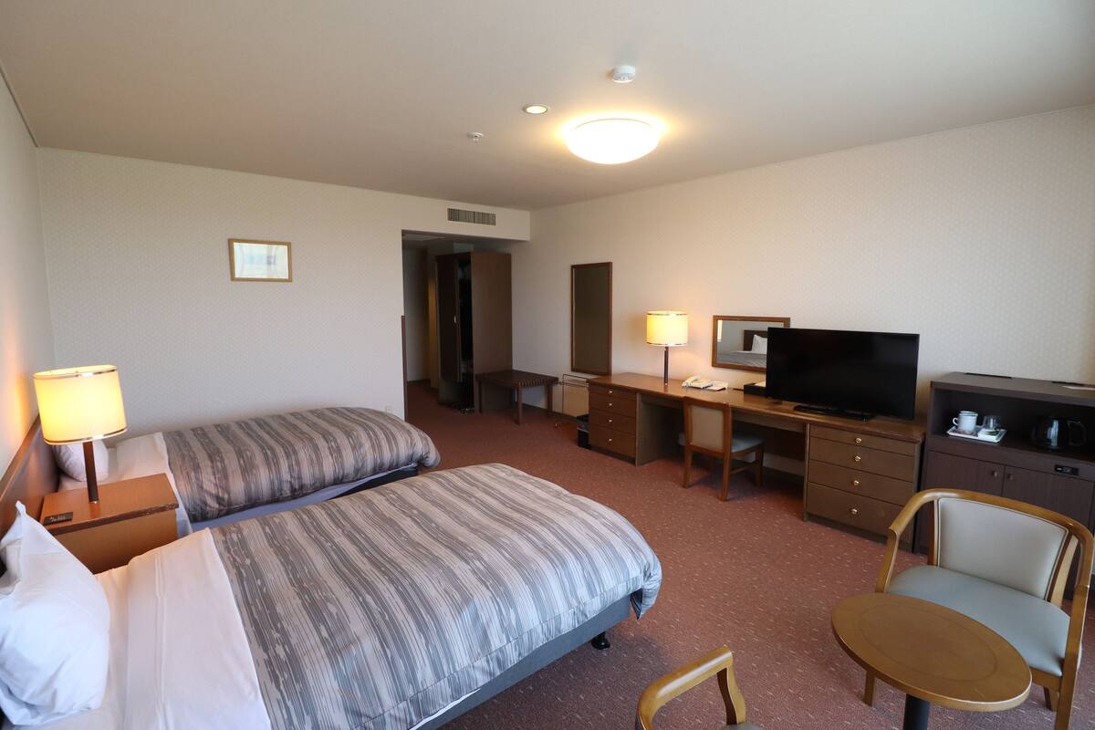 A hotel room with two beds, a desk, a chair, a television, and a lamp.