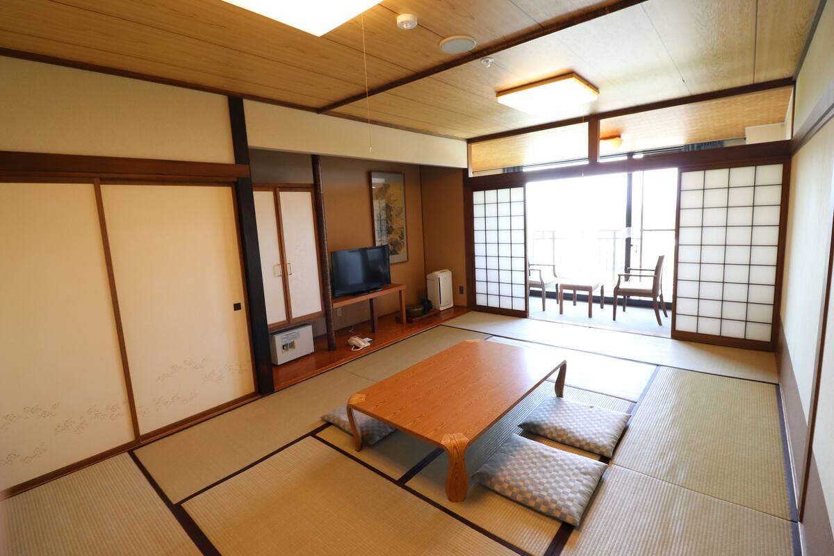 A traditional Japanese room with tatami flooring, a low wooden table, a television, and sliding doors.