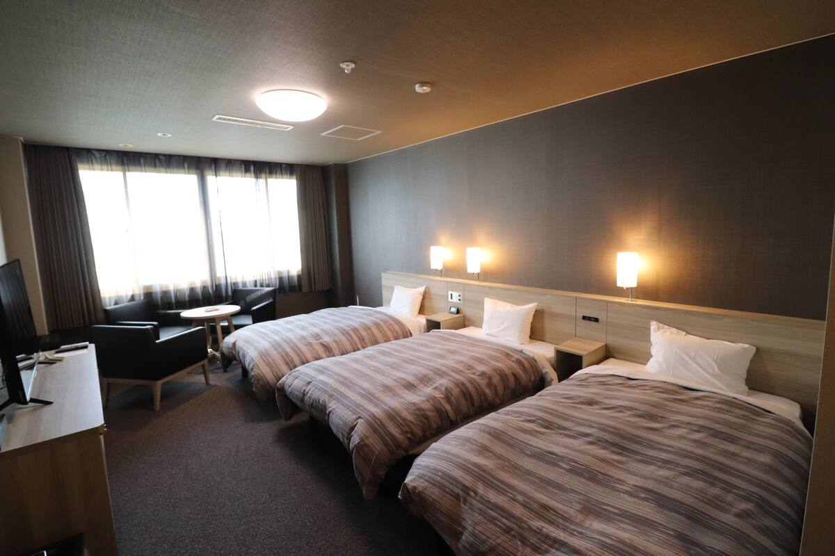 A hotel room with two beds, a desk, a chair, and a TV.
