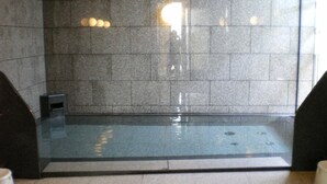 A modern indoor swimming pool with a glass bottom, surrounded by stone walls and a tiled floor. - Hotel Route Inn Tomakomai Ekimae (Tomakomai)