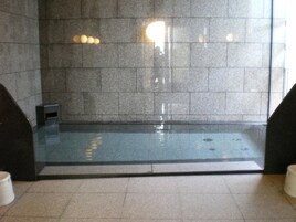 Una piscina interior moderna con fondo de cristal, rodeada de muros de piedra y suelo de baldosas.