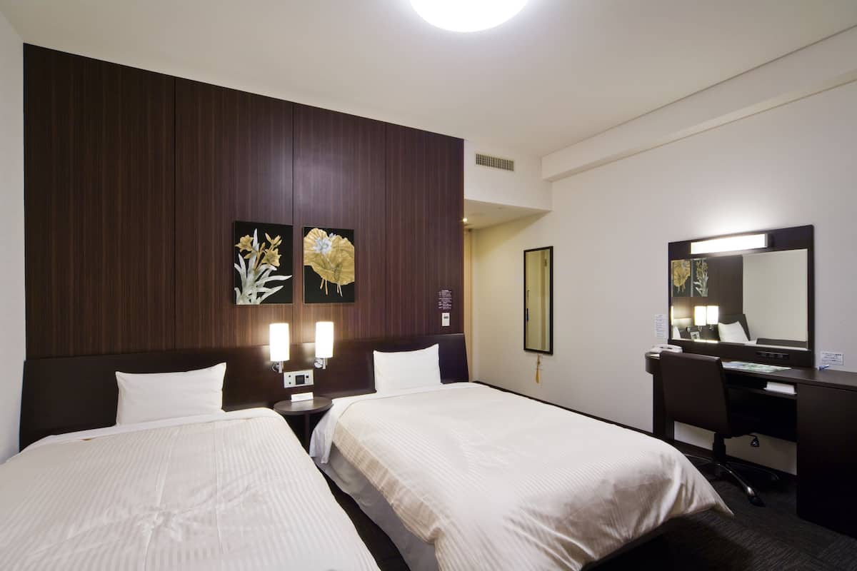 Habitación de hotel con dos camas, un escritorio, una silla, una lámpara de escritorio y un espejo grande.