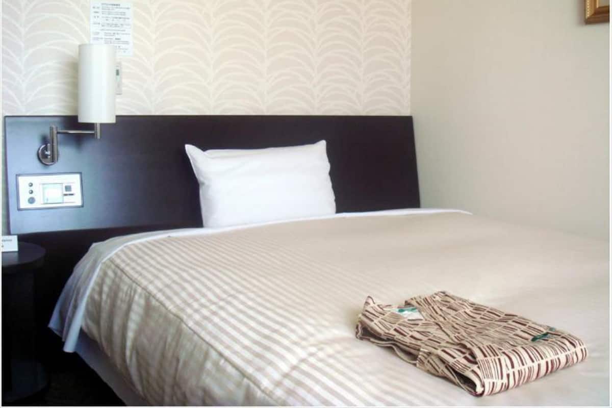 Habitación de hotel con cama, mesita de noche, purificador de aire montado en la pared y papel tapiz estampado.