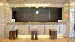 A reception area with a marble counter, two wooden stools, a clock, and a sign indicating an elevator. - Hotel Route Inn Tomakomai Ekimae (Tomakomai)
