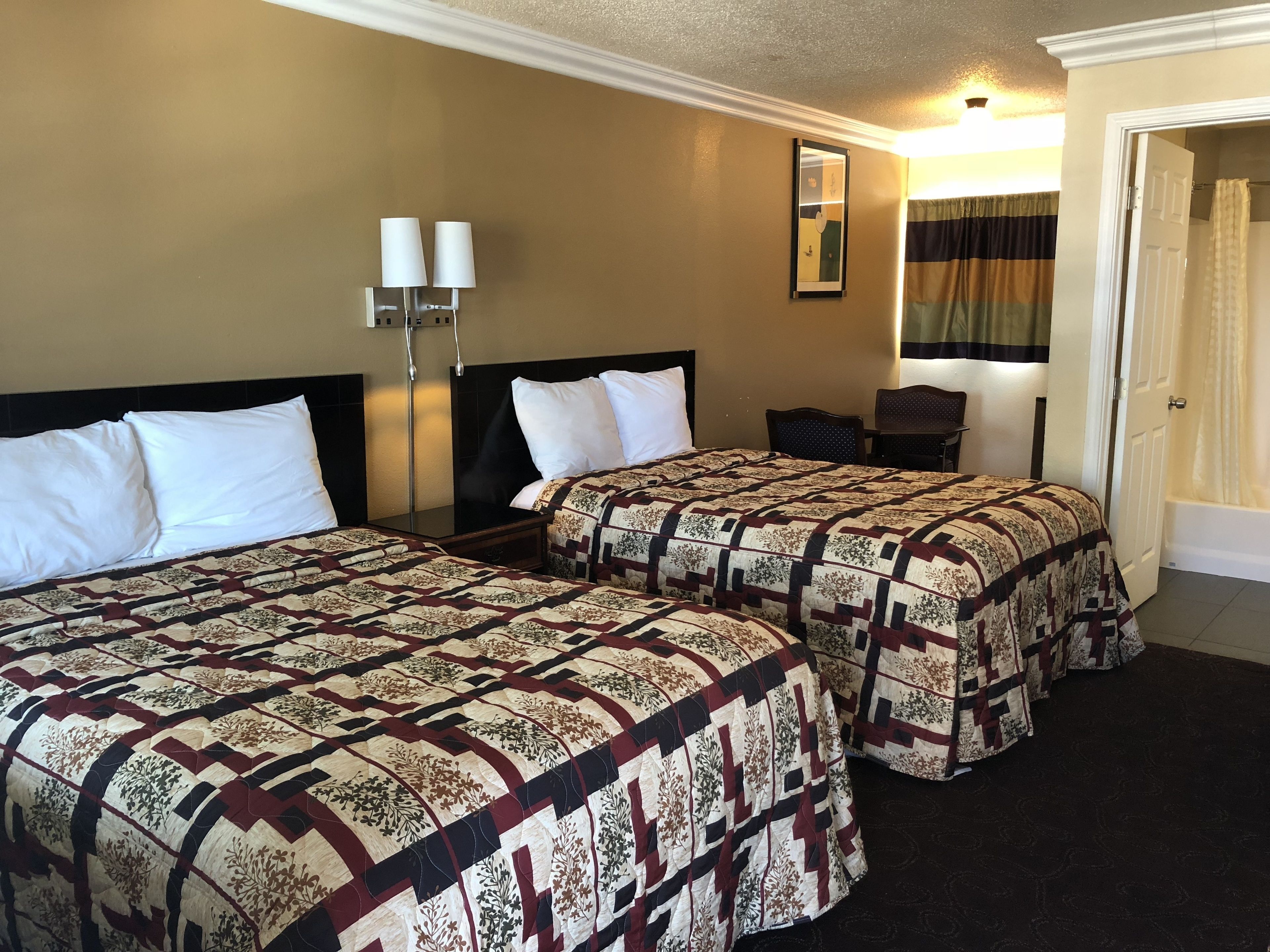 Habitación de hotel con dos camas, una mesita de noche, una silla, un espejo y una puerta.