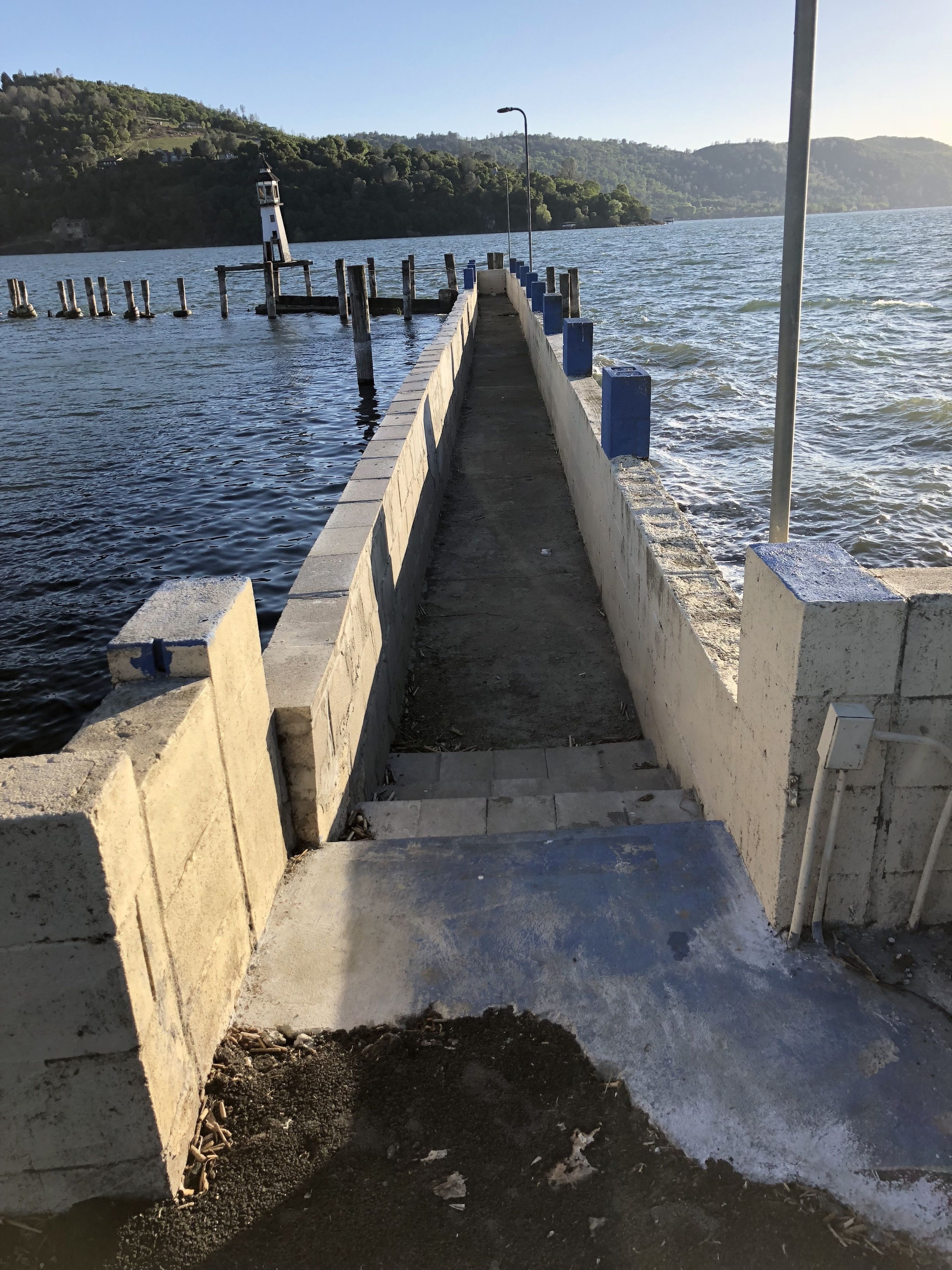 A concrete pier extending into a body of water with a lighthouse at the end.