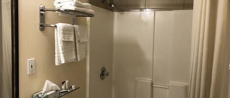 Une salle de bain comprenant des toilettes, une étagère en verre avec des articles de toilette, un porte-serviettes avec des serviettes et une douche avec un rideau.