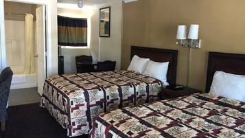 A hotel room with two beds, a desk, a chair, a nightstand, a lamp, and a bathroom with a shower curtain.