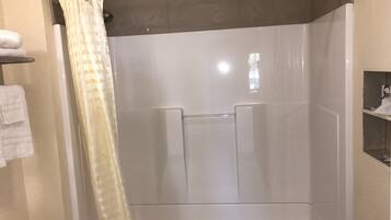 A shower area with a glass door, a towel rack, and a shelf with toiletries.