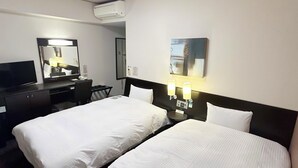 Camera d'albergo con due letti, una scrivania con sedia, una televisione, un condizionatore d'aria e lampade a parete.