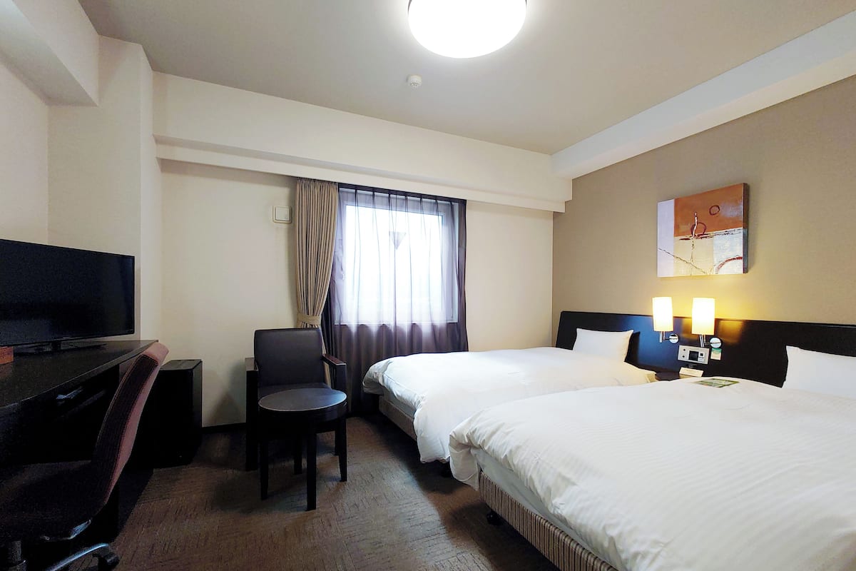 Quarto de hotel com cama, secretária com televisão, cadeira e janela com cortinas.
