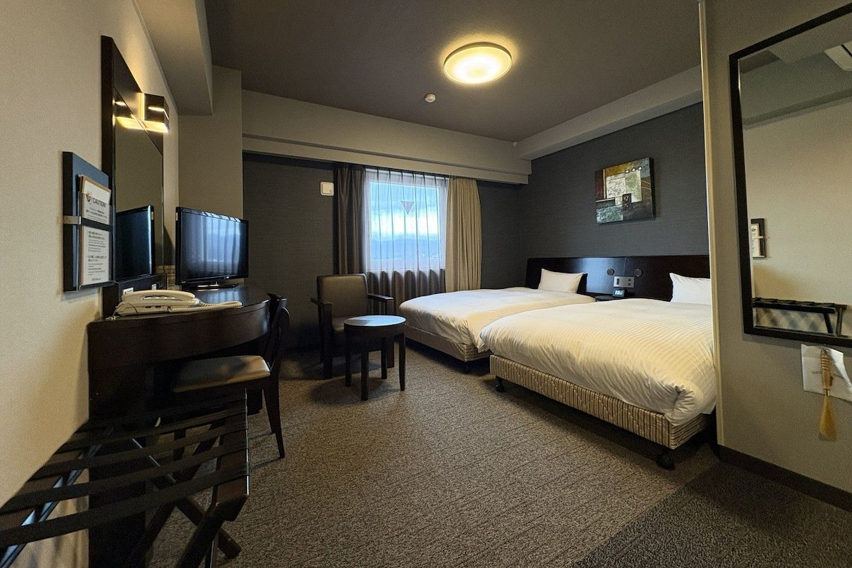 A hotel room with a desk, two beds, a television, and a large mirror.
