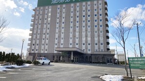 Un hotel a più piani con una targa verde, un parcheggio con un'auto bianca e un cielo sereno.